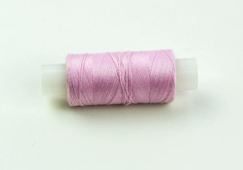 Spool of pink thread for sewing on a white background.