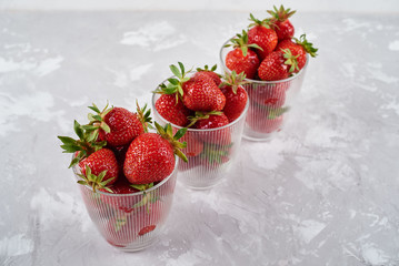 Red ripe strawberries in glass bowls on gray table background, copy space. Healthy food concept
