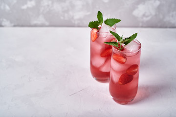 Fresh strawberry lemonade with ice and mint in glass on table, copy space. Cold summer drink. Sparkling glasses with berry cocktail