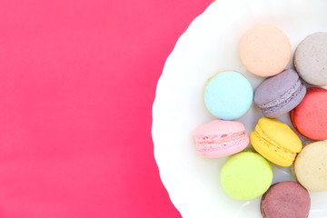Closeup top view of colorful macaron pile in white dish on pink background. Flat lay style. Have copy space.
