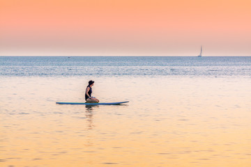 Surfer girl sitting on a surf board and looking into the horizon