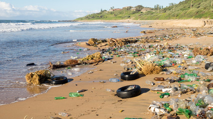 Plastic waste products and car tyres litter a beautiful sandy beach at Umkomaas in South Africa.