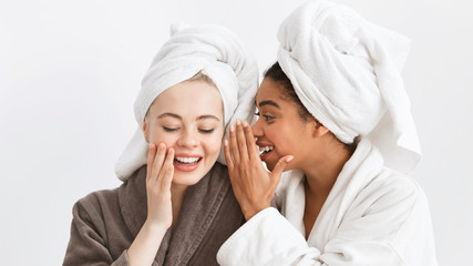 Afro girl in bathrobe sharing secrets with her girlfriend