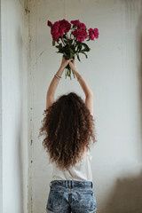 Girl in jeans shorts and silk top with bunch of peony in her hands, back view - 329297668