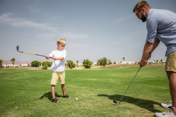Father has fun and teaches his son to play golf on the green grass.