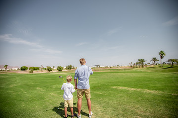 Father has fun and teaches his son to play golf on the green grass.