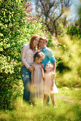 family with daughters stand among the lilac bushes