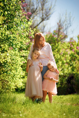 a mom with daughters stand among the lilac bushes