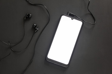 A smartphone with a white screen lies on a black background with stuck headphones.