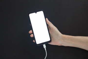 Hand holds a charging smartphone with a light screen on a black background.