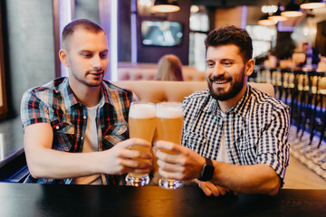 People, men, leisure, friendship and celebration concept - happy male friends drinking beer and clinking glasses at bar or pub