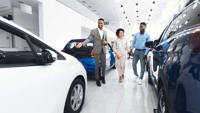 Manager Showing Luxury Automobile To Spouses In Car Dealership Center