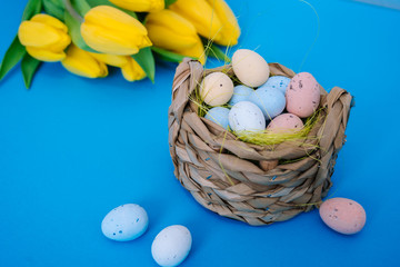 Happy Easter. Easter holiday decorations on trendy colored classic blue background. Creative spring composition with Easter elements - flowers and eggs in basket. Celebrating Easter concept at spring.