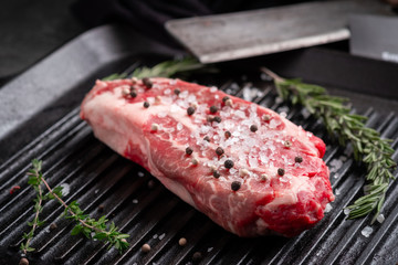 One Perfect raw steak Chuck roll of beef on a black pan with a grill with rosemary, salt and pepper