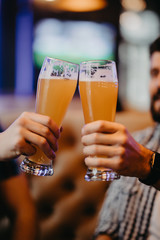 Close up of hands of two friends toasting with glasses of light beer at the pub.