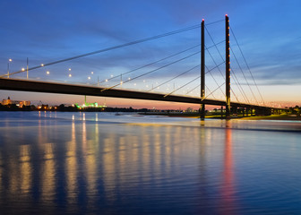 Fototapeta na wymiar Düsseldorf Rheinkniebrücke Rhein Sonnenuntergang Langzeitbelichtung Landeshauptstadt Altstadt Spiegelung Farben Lichter Verkehr Schifffahrt Autos Oberkassel Hafen Fluss Strom bedeutend