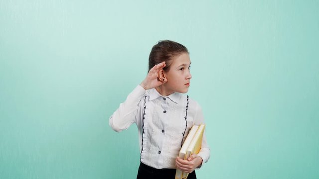 I dont hear you talking. Portrait of a young girl with books in hand, putting hand in ear, asking someone to repeat or listen to bad news, isolated blue wall background.