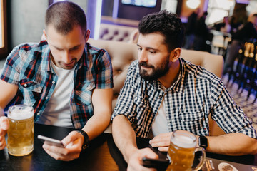 Cheerful old friends having fun with smartphone and drinking draft beer in pub.