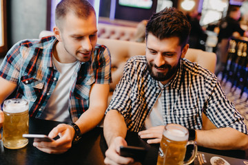 Cheerful old friends having fun with smartphone and drinking draft beer in pub.