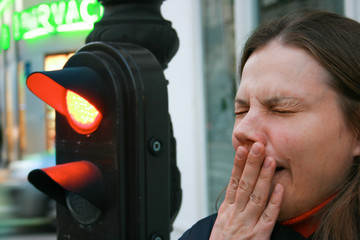 Close-up of a woman yawning in the street next to a traffic light. At the traffic light, a red...
