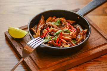 Pork ear snack in a pan. Spicy meat grilled pork served in a frying pan on rustic wooden cutting board.