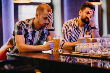 Upset male friends watching sport game or football match and drinking beer at bar or pub