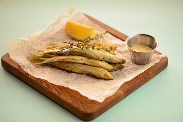 Fried fish gobies in batter with lemon and sauce on a wooden tray, cutting board over light pastel mint green background