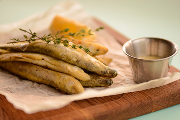 Fried fish gobies in batter with lemon and sauce on a wooden tray, cutting board over light pastel mint green background