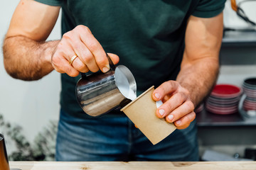 Close-up view of barista holding cup with espresso and pouring foamed milk over it while making cappuccino