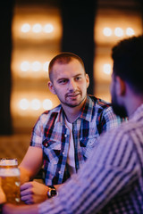 Having a pint with friend. Two cheerful young men in shirt and tie toasting with beer while sitting together at the bar counter