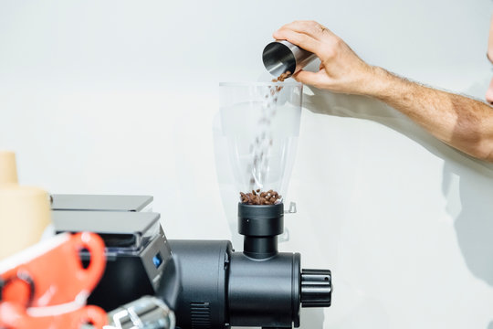 Close-up view of barista putting coffee beans into bean hopper of espresso grinder