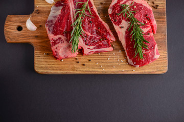 Fresh raw steak on wooden cutting board over black background with spices, top view.