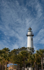 A white brick lighthouse under clear blue skies beyond a green park