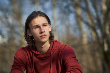 Portrait of a concerned young man sitting in a forest gazing troubled into the distance.