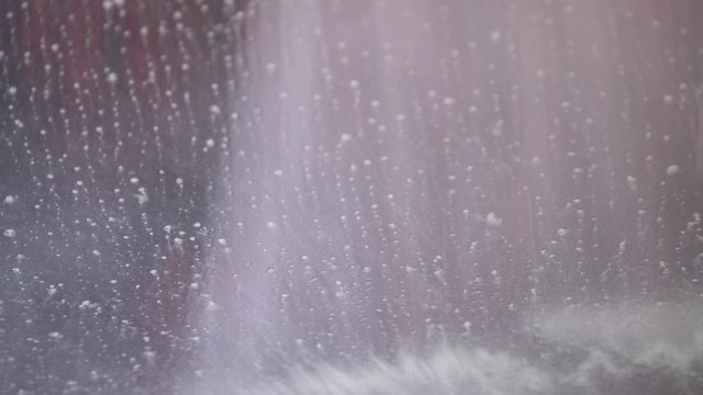 Close up view from inside the car in conveyor tunnel car wash. Washing car with soap and water, rotating brush in automatic car wash service