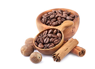 Obraz premium Coffee beans in a wooden spoon with cinnamon and nutmeg on white background.