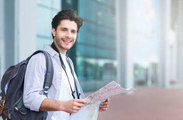 Tourism, vacation, travelling concept. Happy tourist holding map, standing near airport