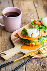 Toast with poached egg, avocado, arugula, cheese, red fish with herbs. Tasty lunch. Proper nutrition with healthy fats. Delicious toast with avocado. Eggs of Benidict. Poached egg spreads on toast