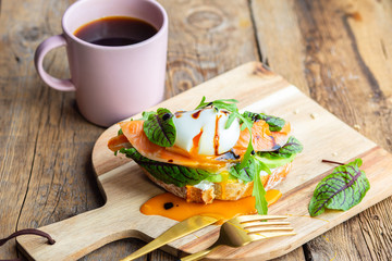 Toast with poached egg, avocado, arugula, cheese, red fish with herbs. Tasty lunch. Proper nutrition with healthy fats. Delicious toast with avocado. Eggs of Benidict. Poached egg spreads on toast