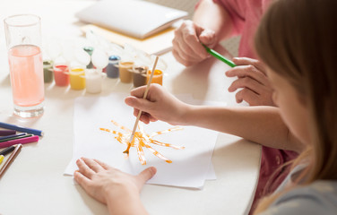 Little girl and her grandmother painting together at table, closeup view