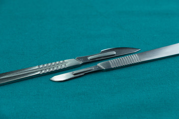 Surgical instrument, stainless steel scalpel handle number 3 with blade number 10 and scalpel handle number 4 with blade number 24 on surgical green drape fabric.
