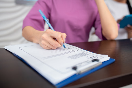 Receptionist wearing purple uniform holding pen while making notes
