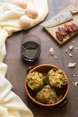 Carciofi imbottiti su sfondo in legno. Sul retro salsiccia affettata e un bicchiere di vino. Molliche di pane sulla scena