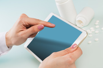 doctor's hands in a white medical coat use a tablet, two white jars of pills and a red heart on a blue background. concept of medicine, cardiology