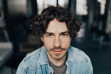 Fototapeta premium Close up portrait of handsome guy with curly hair in blue jeans shirt looking to camera