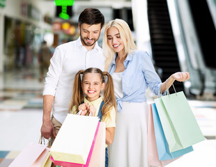 Family Posing In Shopping Mall Holding Colorful Shopper Bags Indoors