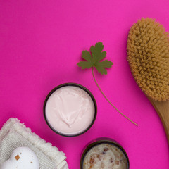Obraz na płótnie Canvas Massage body brush, scrub, salt, mask and green leaf on pink background