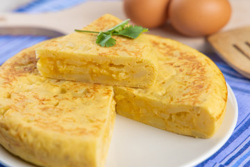 Spanish potato omelette cut on white plate with eggs and wooden spoon
