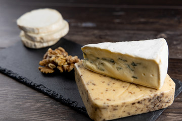 Fresh cheeses of different flavors with nuts on black chalkboard plate and wooden board on white commercial background and space for text