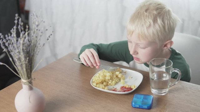 The boy eats pasta with a meatball at home for lunch. 